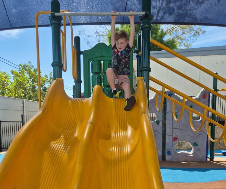 A young boy sits at the top of a slide
