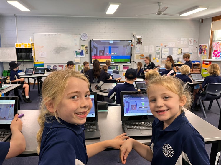 Two young girls work together happily on a computer in a busy, colourful classroom