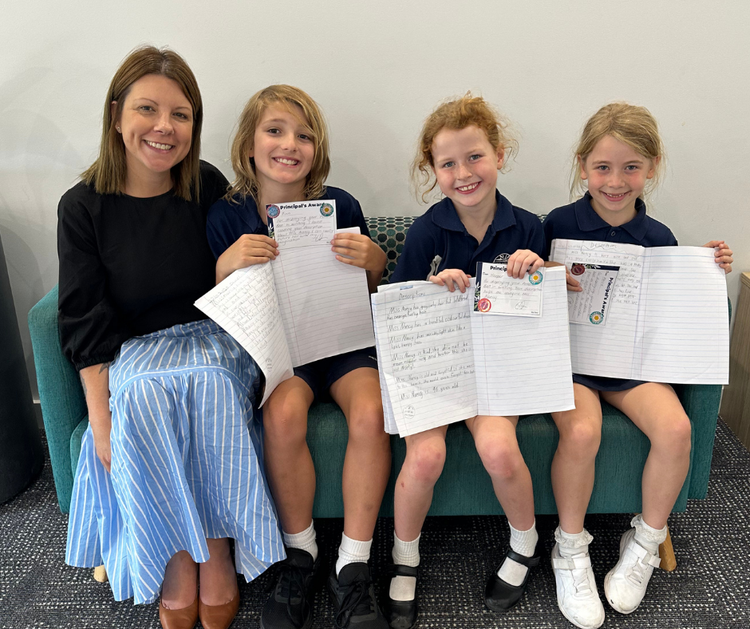 Renee, our principal, sits proudly with three young students who are holding up examples of their beautifully written work