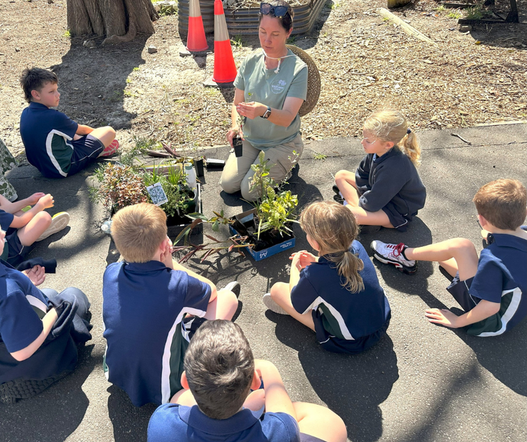 Students gather around a local botanist who is teaching them about the native plants she is holding