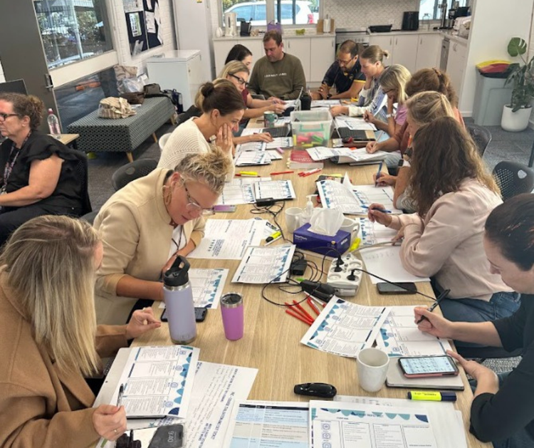 Many staff sit at a long table, working on a Professional Development activity at a Staff Development Day