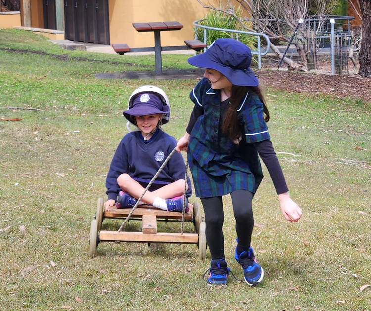 Two girls laugh as one pulls the other on a wooden cart at an excursion